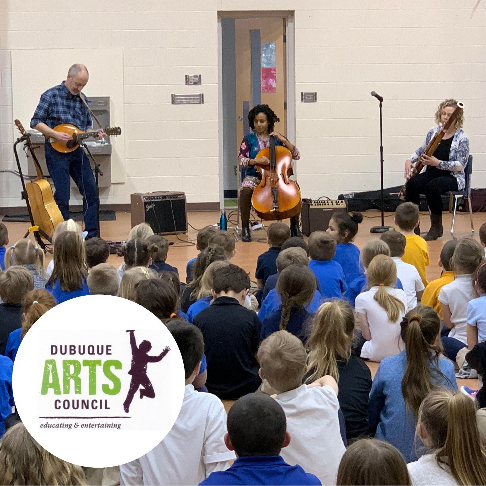 students on gym floor of school watching three music performers